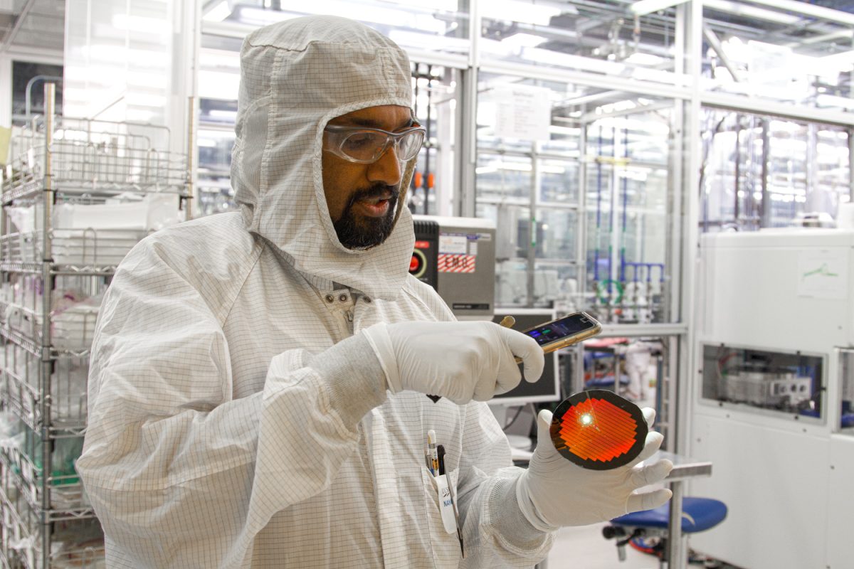 Demis D. John, a UCSB Nano fab scientist illuminates a silicon wafer and produces an iridescent rainbow on Sept. 24, 2024 at the Nano fab lab at UCSB in Santa Barbara, Calif. "The rainbow color is because each of those squares is an array of thousands on 300nm posts... and that's around the same size as the wavelength of light," John explained.